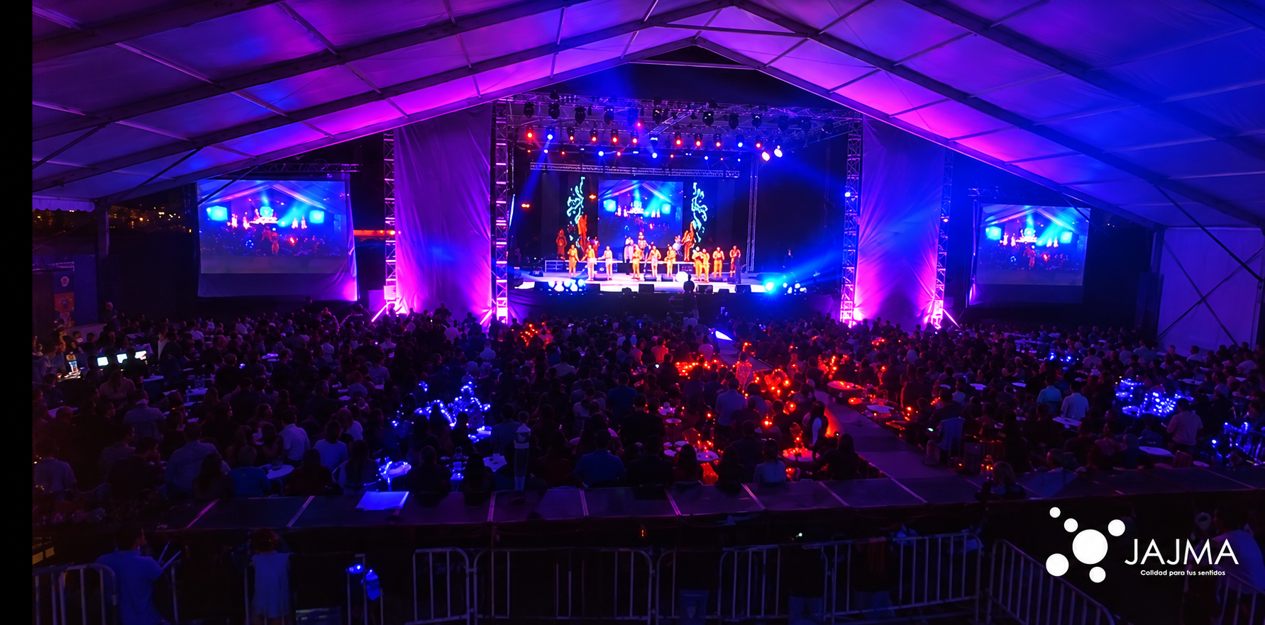 Presentación en vivo con iluminación azul y morada y pantallas laterales.
