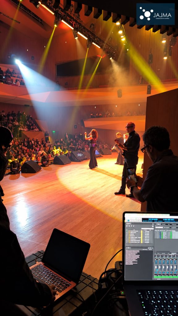 Vista lateral del concierto con público, músicos y puestos de operación técnica.