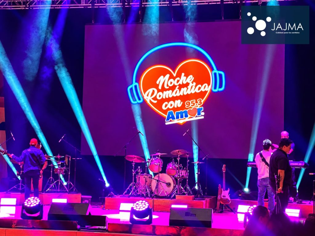 Pantalla de Noche Romántica con Amor 95.3 y haces de luz sobre el escenario.