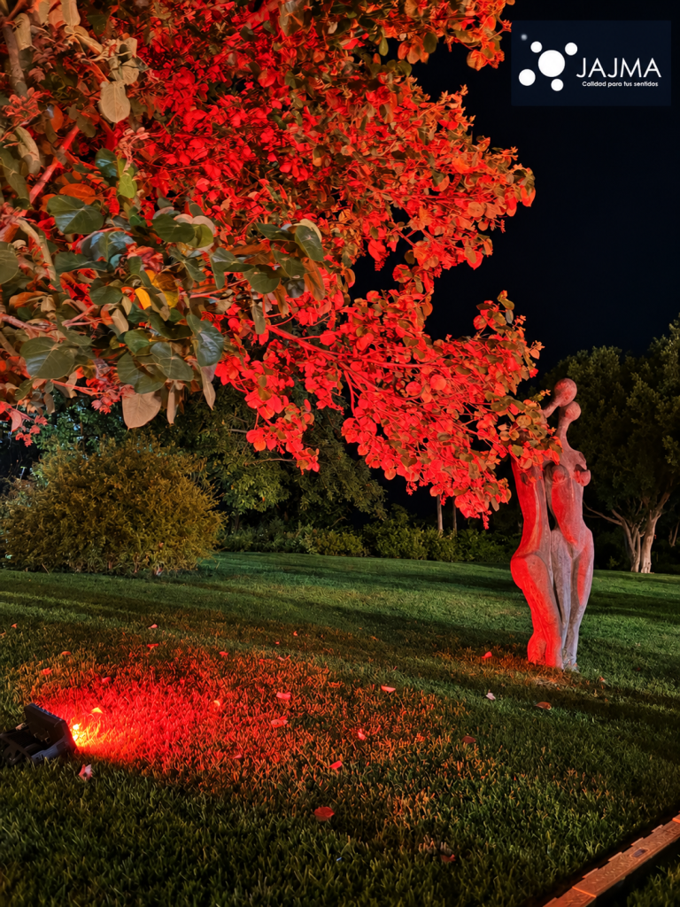 Escultura y follaje iluminados en rojo en los jardines de Vaivén.