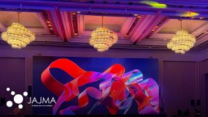 Salón de eventos corporativos con candiles y pantalla LED de gran formato producido por Jajma